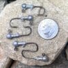 A penny sitting on top of a rock next to some fishing hooks.