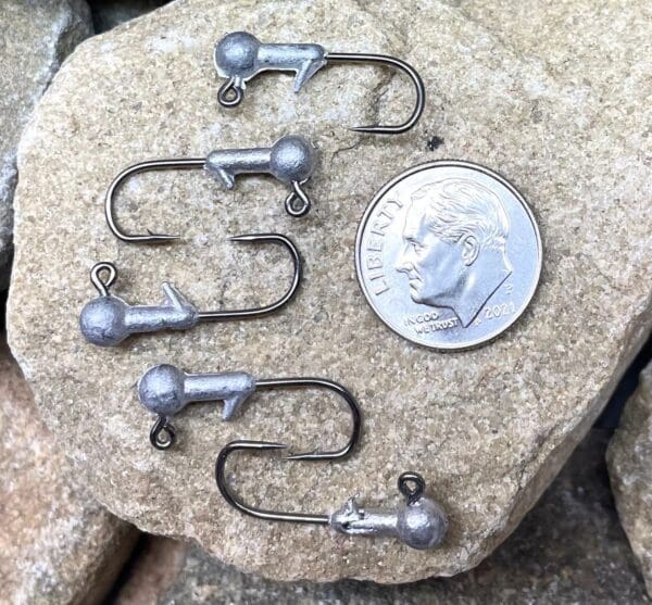 A penny sitting on top of a rock next to some fishing hooks.